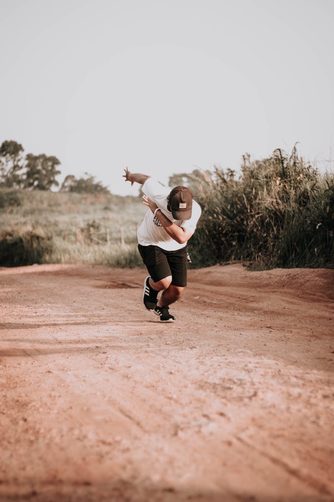 A young man wearing casual attire runs on a dirt path surrounded by nature on a sunny day.