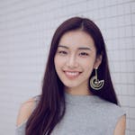 Portrait of a stylish woman with earrings smiling against a white tiled wall.