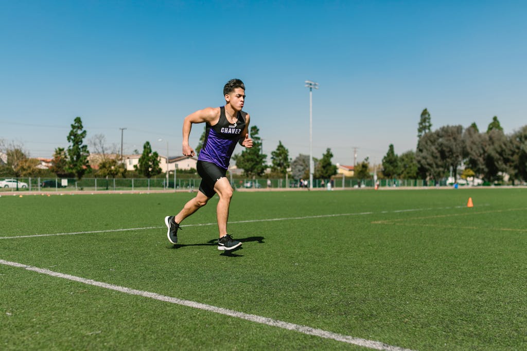 A young man in sportswear running on a grassy outdoor field, capturing dynamic motion and fitness.