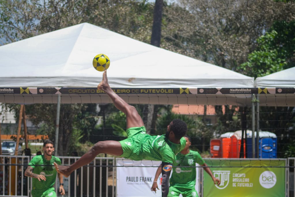 Athletes showcasing futevôlei skills at a sunny tournament in Ilhéus, BA, Brazil.