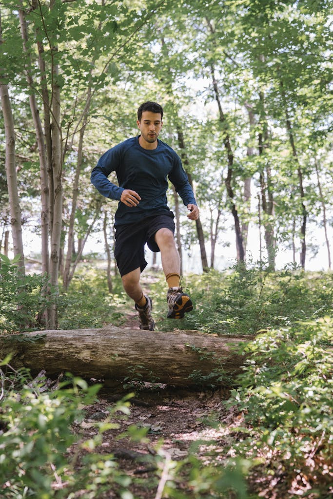 Athletic man jumping over a log during a vibrant forest run in summer.