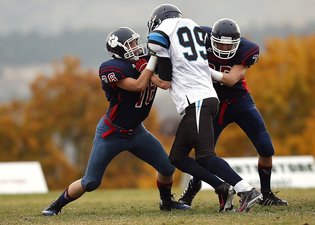 Football players in action during a competitive game on a field with autumn foliage.