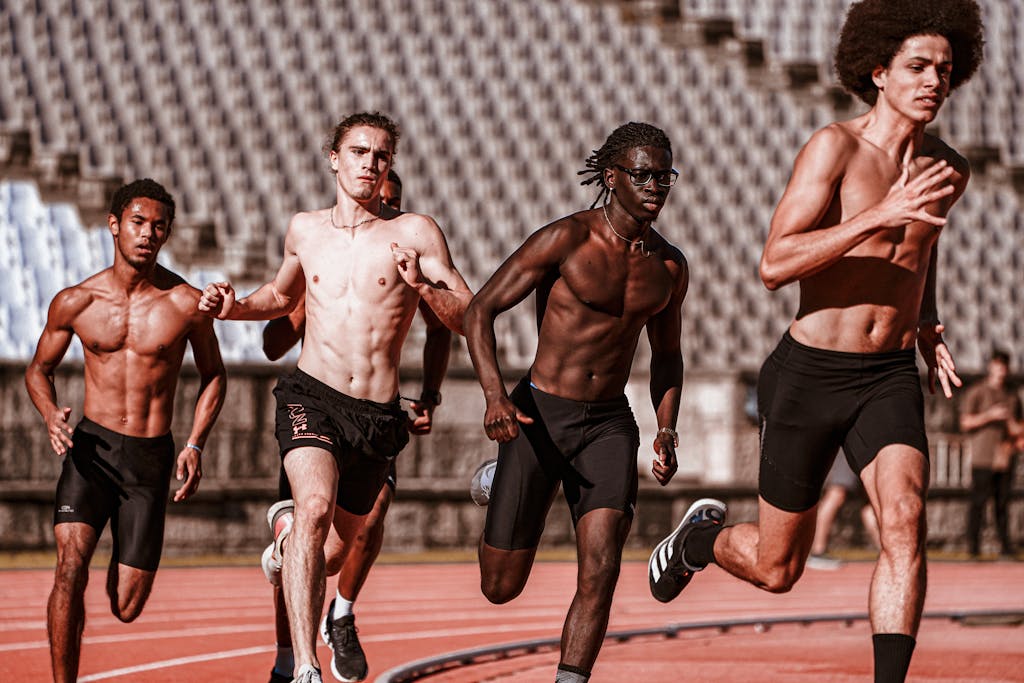 Four athletic men running on a sunny day at an outdoor track race, showcasing diversity.