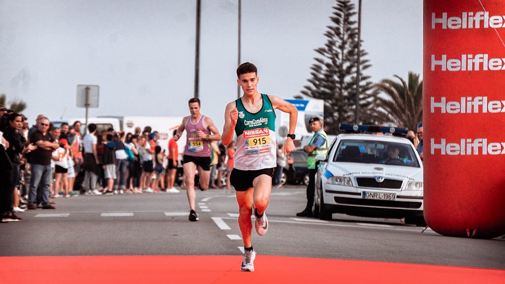 Two male athletes racing in a marathon with a cheering crowd and bright finish line.