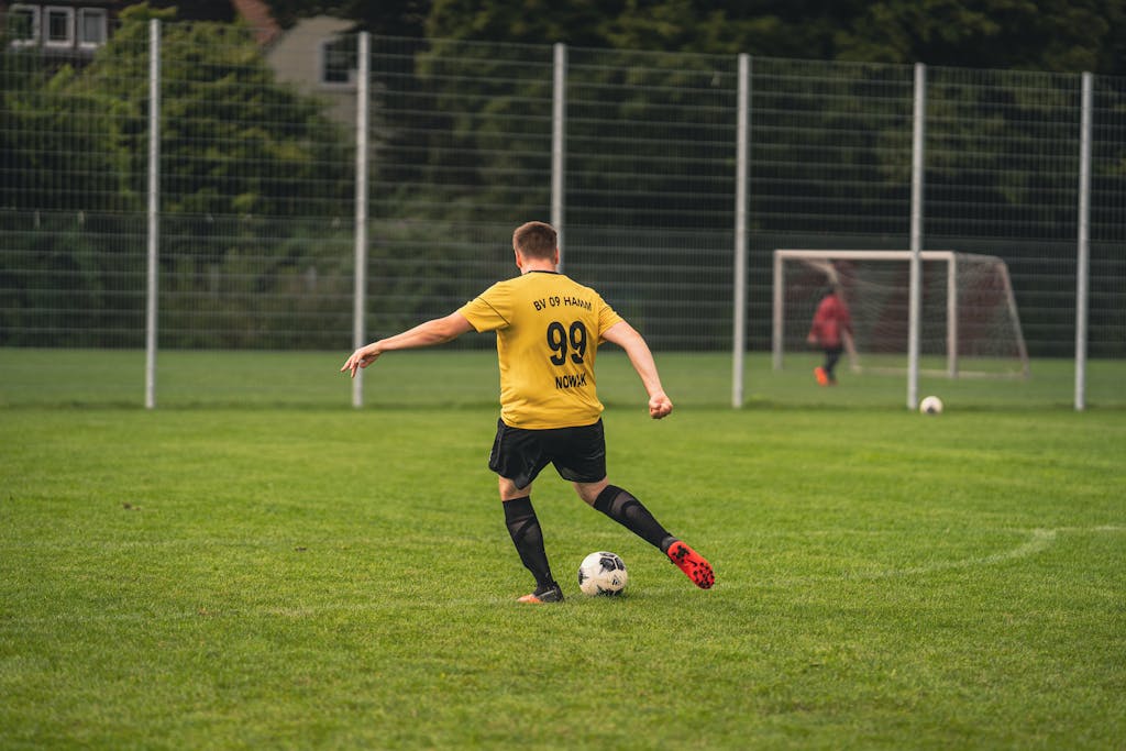 A soccer player in a yellow jersey kicking a ball on a lush green field during the day.