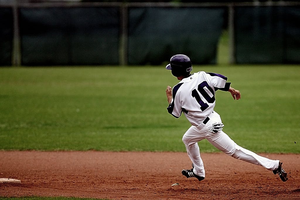 A young baseball player in uniform sprints towards base on a sunny day.