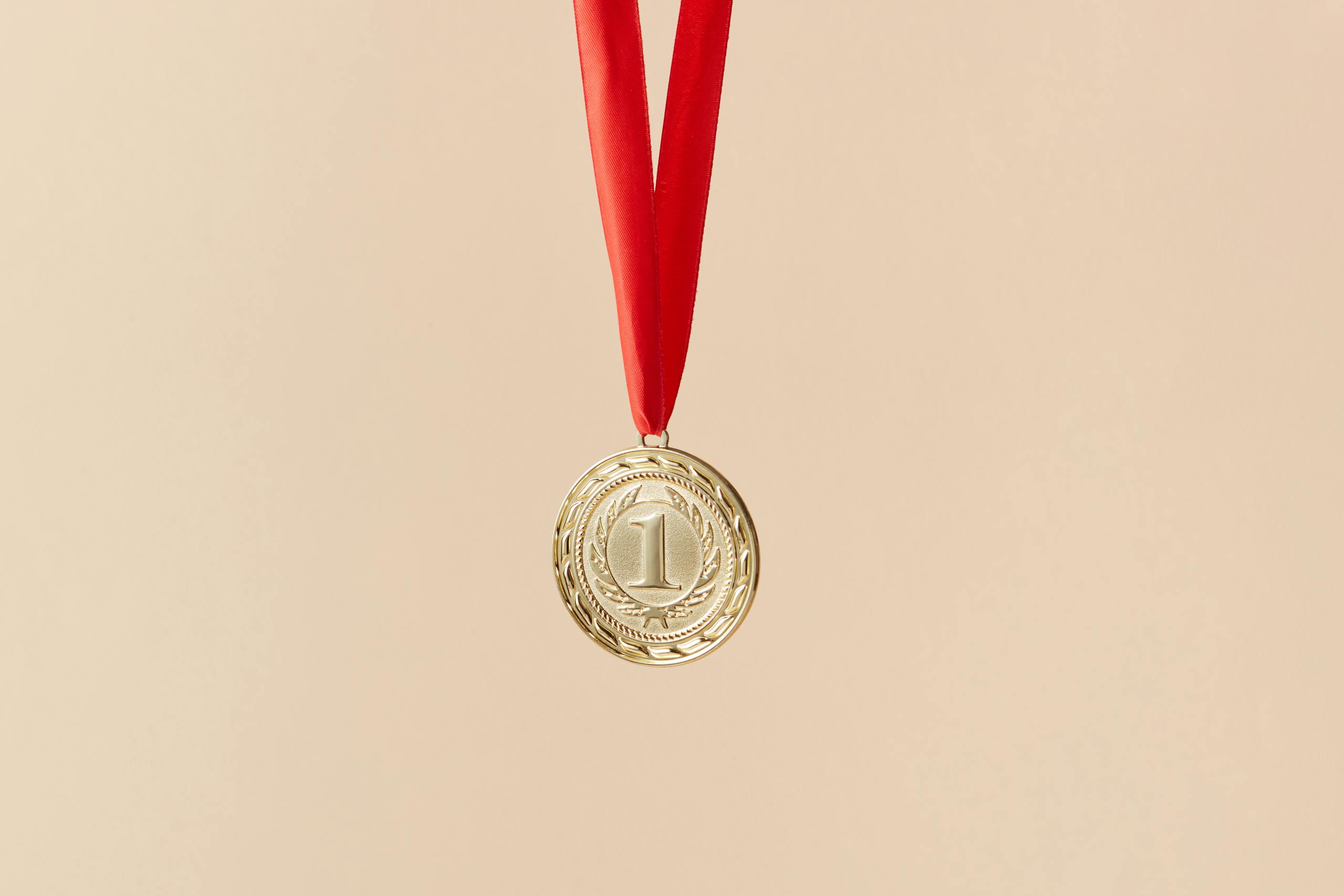 Close-up of a gold medal with a red ribbon on a beige background, symbolizing achievement.