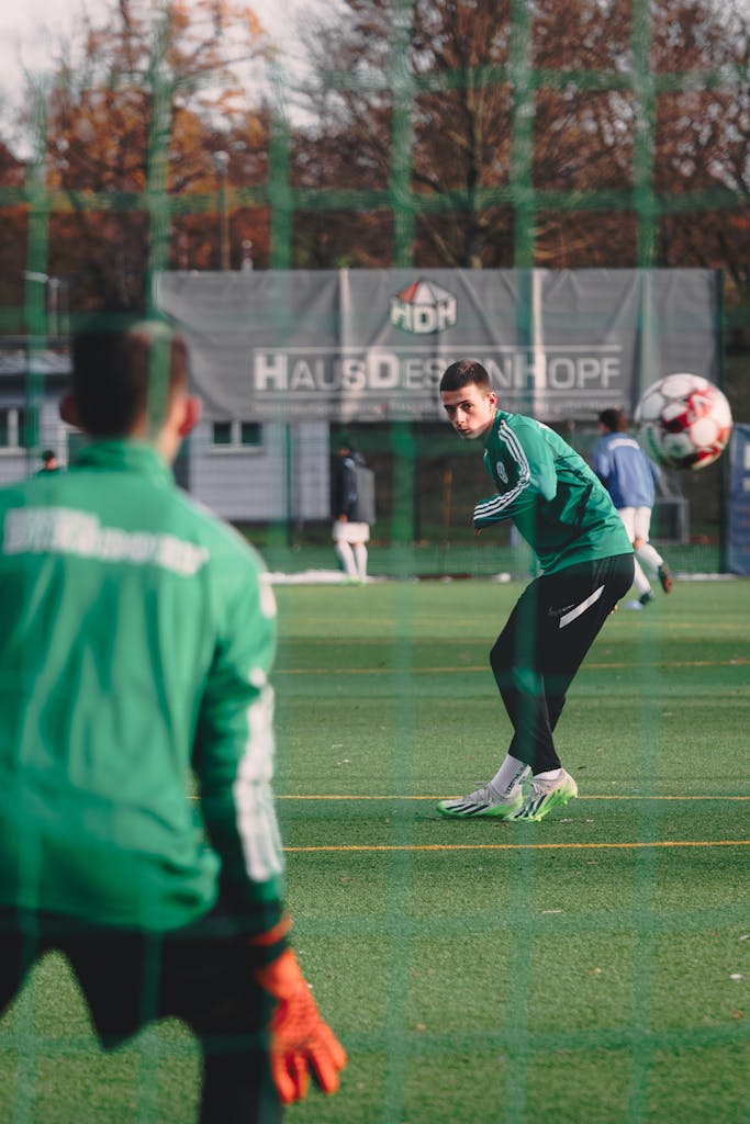 Two men training soccer on an outdoor field during autumn, focusing on goalkeeping skills.